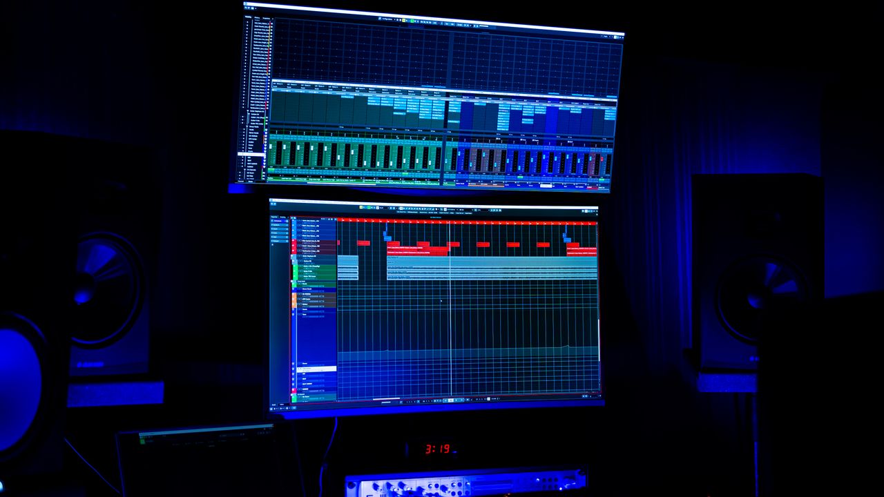 services-05 A modern recording studio featuring two screens displaying audio editing software under blue neon lighting.