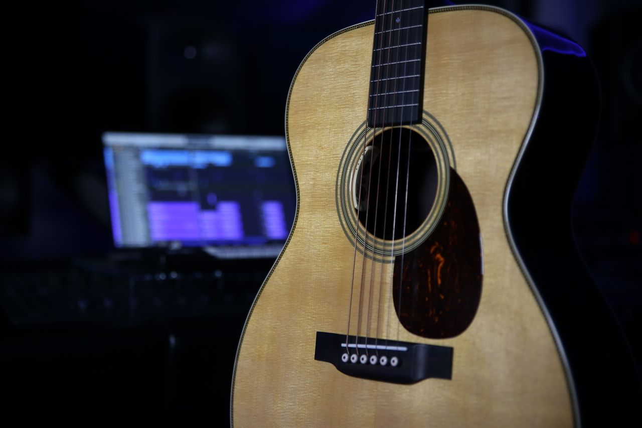 missions-03 Close-up of an acoustic guitar in a modern home studio environment with dim lighting.