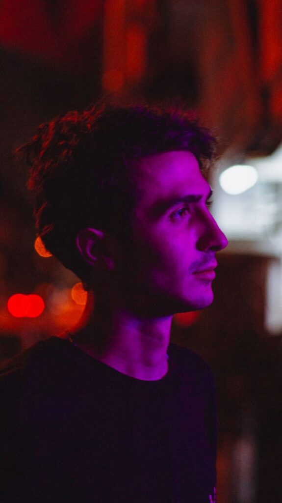 pexels photo 18193930 18193930 Profile of a young man at night highlighted by purple neon lighting, creating a moody atmosphere.