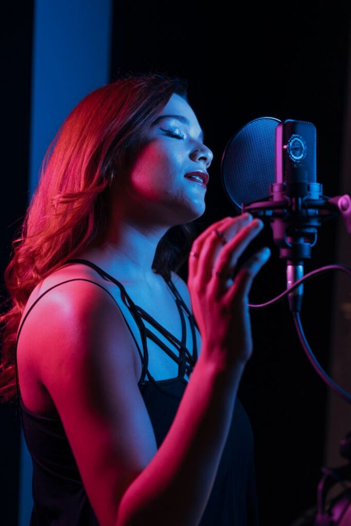 Young female singer in a recording studio, passionately singing into a microphone with closed eyes.
