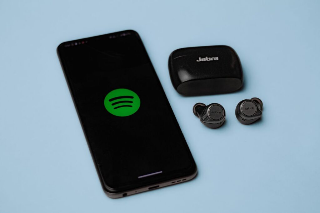 Closeup of Jabra true wireless earbuds with a smartphone displaying the Spotify app on a blue background.